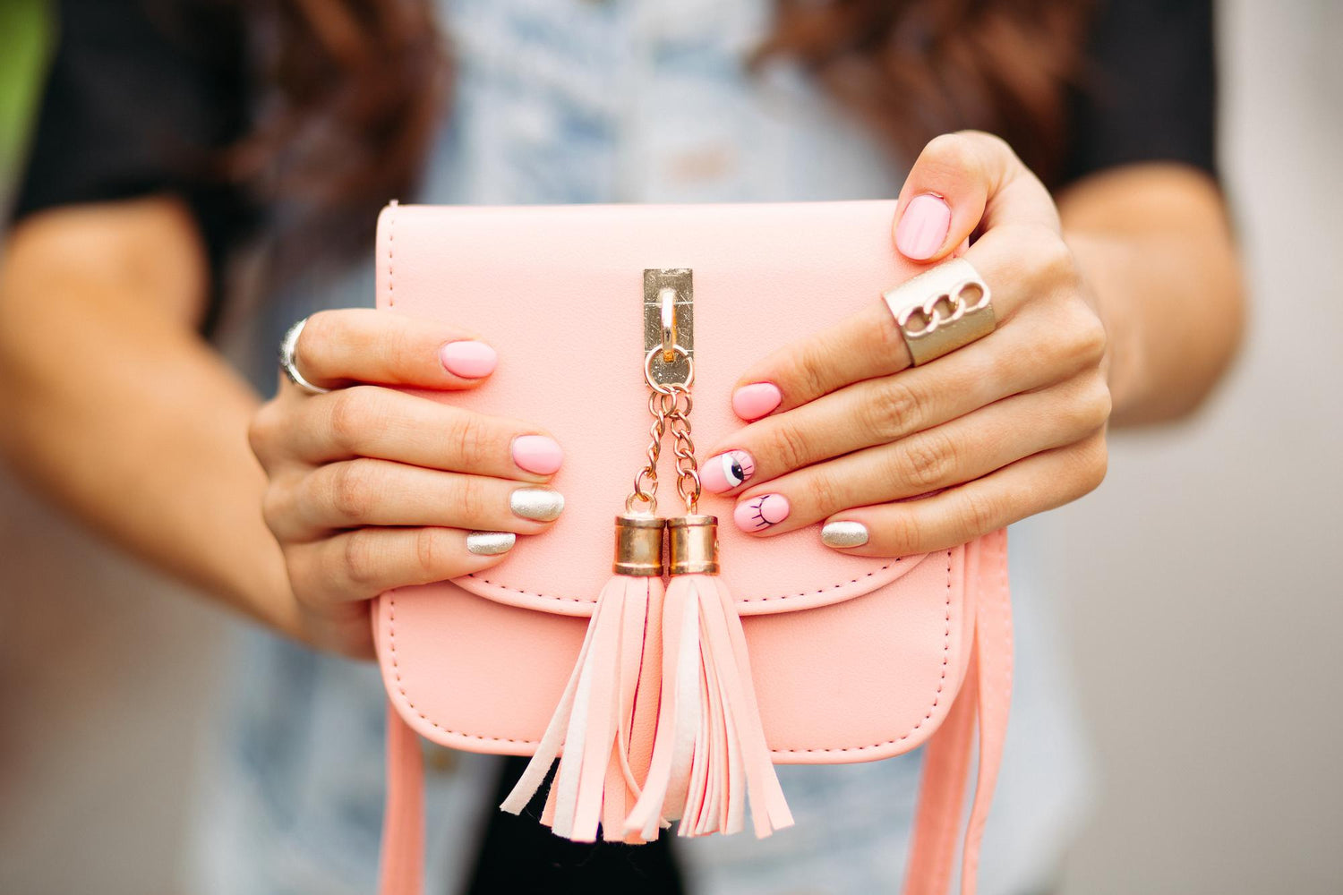 Femme ayant fait une manucure rose et dorée qui tient un sac à main rose